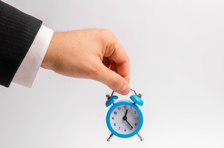 A businessman's hand holds a blue alarm clock on a white background. The concept of the flow of...