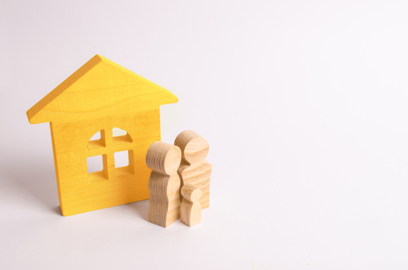 Figures of people stand near a wooden house on a white background. A young family is standing near their house. The concept of buying a home. The property. Family happiness. Unit of society.の写真素材