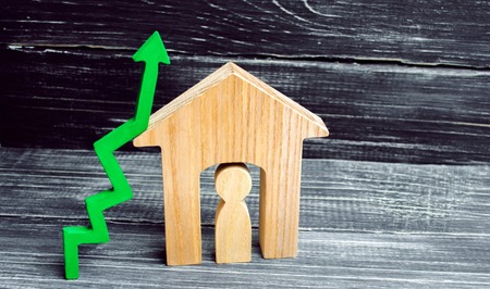 wooden house with a man inside. green arrow up. concept of high demand for real estate. increase energy efficiency of housing. rise in house prices. property. population growth. place for textの写真素材