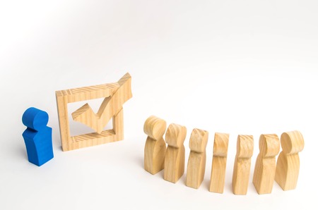 Wooden human figures stand in a row next to government building in the box. Concept of elections and social technologies. Volunteers, parties, candidates, constituency electorates. Selective focusの写真素材