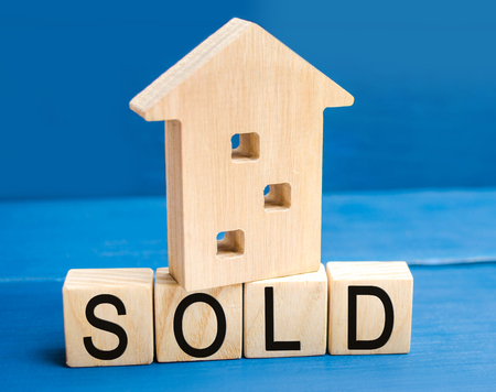 wooden house on a blue background with the inscription sold. sale of property, home, real estate. affordable housing. place for text. copy spaceの写真素材