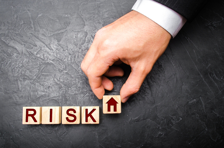 The realtor's hand stretches a cube with a house pattern to the word risk. The concept of risk, loss of real estate. Property insurance. Loans secured by home, apartment. Financial risks, litigation.の写真素材