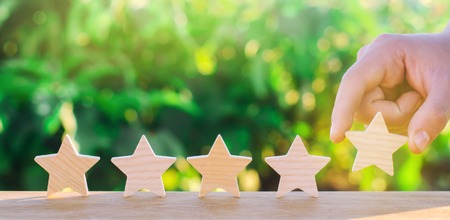 Hand puts the fifth wooden star. Get the fifth star. The concept of the rating of hotels and restaurants, the evaluation of critics and visitors. Quality level, good service. selective focusの写真素材
