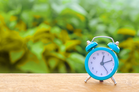 The blue alarm clock indicates the beginning of the first on a green bokeh background. time management. concept of the flow of time. copy space. minimalist style.の写真素材