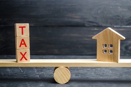 Wooden house with the inscription "Tax" on the scales. Taxes on real estate, payment. Penalty, arrears. Register of taxpayers for property. Law-abiding, evasion of payment. Court lawの写真素材