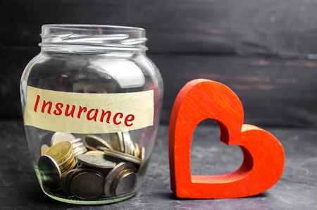 Glass jar with coins and the inscription "Insurance". The concept of medical insurance of life, family, health. Healthcare. Red heartの写真素材