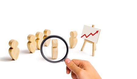 Magnifying glass is looking at the Wooden figures of people stand in the formation and listen to...