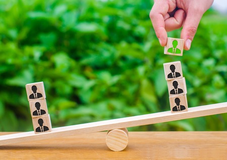 The hand adds a cube with the image of the employee to the stack on the scales. The concept of hiring employees and the appointment of the leader and leader of the team. Business management personnel.の写真素材
