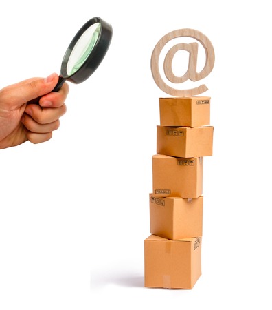 Magnifying glass is looking at the tower of cardboard boxes and an email symbol on top. concept of online sales, shopping and online shopping. Realization of goods and services through the Internetの写真素材