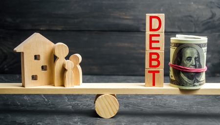 Glass jar with coins and the inscription " Debt ", family and wooden house. Real estate, home savings, loans market concept. Payment of real estate tax. Mortgage. Risks of buying a house. Foreclosureの写真素材