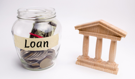 Glass jar with coins and the word Loan and a state building. Borrow money, Take a loan or a credit from a bank. Deposit concept. Financial management and successful credit.の写真素材