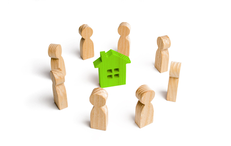 Wooden figurines of people stand around a green house. Search for a new home and real estate. Buying or selling a home. Moving to a new home. Rent or construction. Buying a property. Investmentsの写真素材