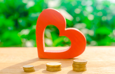 Red wooden heart and money. The concept of saving and accumulation money. Health charity. Donation. The purchases of Valentine's Day. Soft selective focus on the coinsの写真素材