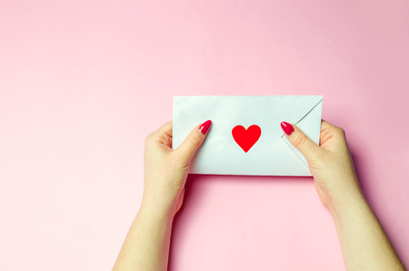 Female hand holding an envelope with a red heart. A love letter to the beloved. Valentines day...