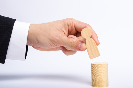 A man's hand puts a person's figure on top of his new post. A businessman appoints a person to a managerial position. Recruitment and leadership position. Human resources, headhuntersの写真素材