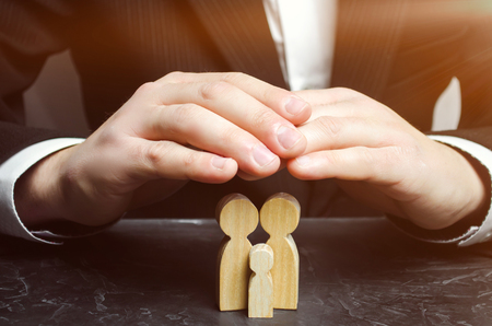 Insurance agent holds hands over family. The concept of insurance of family life and property. Family care and helping hand concept. Health insurance. Health care. Security and Property Protectionの写真素材