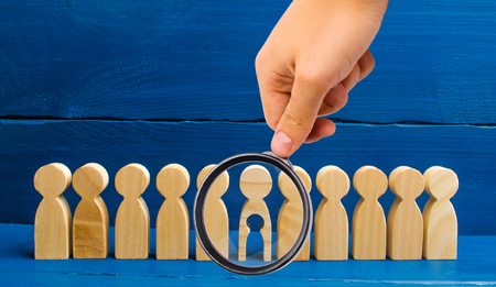 Magnifying glass is looking at the wooden figure of people with a void inside the body in the form of a child stands in line with other people. The concept of infertility and the loss of a child.の写真素材