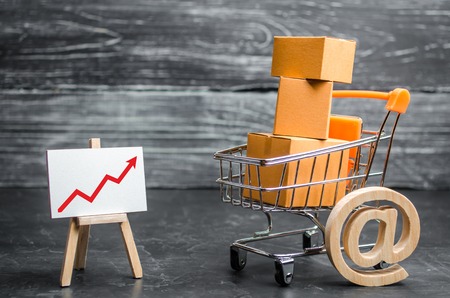 A supermarket cart loaded with lots of boxes and a red up arrow. Online sales and e-commerce, product and brand promotion. concept of increasing sales, increasing consumer ability, welfare of societyの写真素材