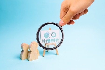 Magnifying glass is looking at the People stand near the canvas with graphs and reports. Concept of business processes, presentations and staff briefing. Business report, summary and planning.の写真素材
