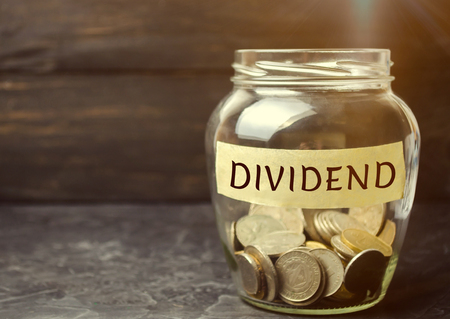 Glass jar with the word Dividend. A dividend is a payment made by a corporation to its shareholders as a distribution of profits. Concept business finance and investment. Saving money. Dividend taxの写真素材