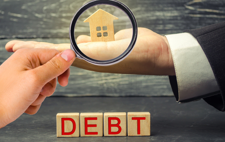 Miniature wooden house and the inscription " Debt ". Real estate, home savings, loans market concept. Payment of real estate tax. Mortgage. Risks of buying a house. Foreclosureの写真素材