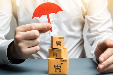 A man holding an umbrella above the boxes. Insurance of purchases and parcels, money back guarantee and non-damage to the goods upon shipment. Internet trade, commerce, market. Free trade zone.の写真素材