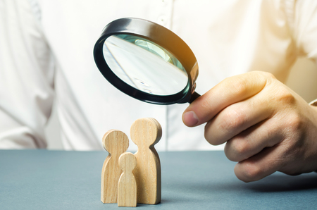 A person looks at family figures through a magnifying glass. The study of family composition, statistics. Birth control and juvenile police. The study of society and the behavior. Marketing.の写真素材
