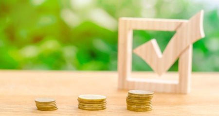 Wooden check mark and stacks of coins. Lobbying the adoption of regulations and laws. Illegal money laundering and control of financial flows. Interest rates on deposits and loans. Selective focusの写真素材