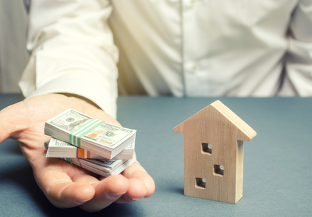 Businessman holds dollars in hands near wooden house. Real estate investment concept. Mortgage. Loan for housing. Credit. Rent. Rental. Buying a property. The accumulation of money. Selling a houseの写真素材