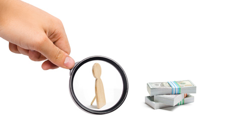 Magnifying glass is looking at a fake human figurine and a pile of money. Shader, unauthorized login and withdrawals. The thief steals funds. The study of sources of profit, money laundering, offshoreの写真素材