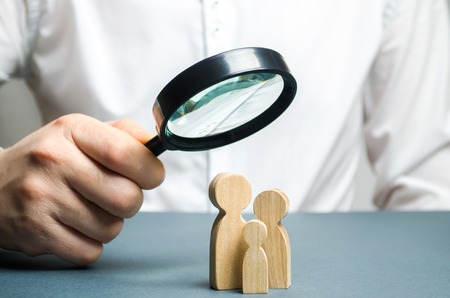 A man looks through a magnifying glass at a family figure. The study of family composition and demographic situation. Statistical data. The program of support for young families, financial assistance.の写真素材