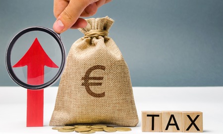 Wooden blocks with the word Tax, up arrow and money bag. The concept of tax growth in the country. Taxes on income, on luxury. Business and Finance. Growing tax on housing and real estate.の写真素材