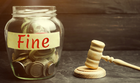 Glass jar with the word Fine and the judge's hammer. Penalty as a punishment for a crime and offense. Financial punishment. Violations of traffic laws. Fraud. Fines can also be used as a form of taxの写真素材