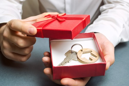Man holds a miniature house in a gift box. Housing as a gift. Win an apartment in the lottery. To inherit property. Holiday discounts. Buying an apartment at a low price. Sale of real estate. Presentの写真素材