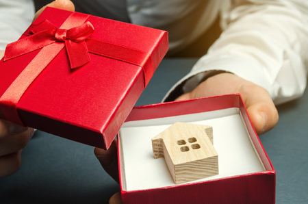 Man holds a miniature house in a gift box. Housing as a gift. Win an apartment in the lottery. To inherit property. Holiday discounts. Buying an apartment at a low price. Sale of real estate. Presentの写真素材