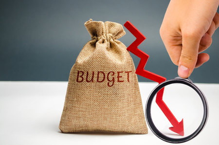 Money bag with word Budget and down arrow. Unsuccessful business and poverty. Profit decline. Loss of investment. Low wages and savings. Economic crisis. fall of the financial marketの写真素材