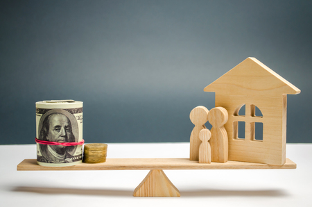 Family and wooden house with money on the scales. The concept of real estate purchase. Sale of property. Payment of the mortgage. Redemption of taxes. Tax refund. Credit for the apartment.の写真素材