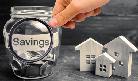 A glass jar with coins and the inscription Savings and houses. The concept of real estate purchase. Buy a house, apartment. Property. Affordable housing. Accumulation. Home rentの写真素材