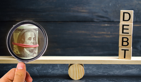 Dollars and the inscription "Debt" are on the scales. Concept of financial crisis and problems. Risk management concept. Payment of taxes. Debt exemption. Balanceの写真素材