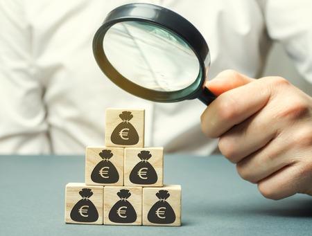 Businessman holds magnifying glass over cubes with euro. Analysis of profits and revenues in the company. Distribution of money. The accumulation of capital. Budget planning. Business conceptの写真素材