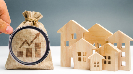 Money bag with chart up and wooden houses. The concept of real estate market growth. The increase in housing prices and rent. Growing demand for property purchase. Rising interest rates on mortgagesの写真素材