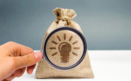 A magnifying glass is looking at a bag with a light bulb image of ideas and inspiration. Generation of innovative business ideas. Creative process. The accumulation of experience and skills.の写真素材