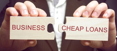 Businessman collects wooden puzzles with the words Business and cheap loans. Cheap and affordable loans to support small and medium businesses. Marshall plan. Stimulate economic growth.の写真素材
