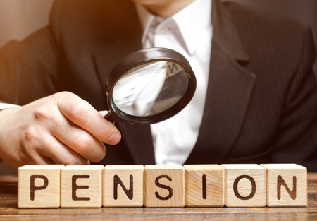 Wooden blocks with the word Pension and a magnifying glass in the hand of a man. Analysis of retirement payments. The size of pensions. Pension Fund. Financial condition of older people. Supplementsの写真素材