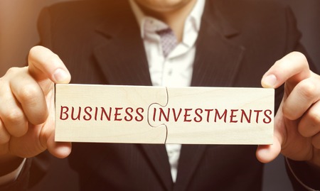 Businessman collects wooden puzzles with the words business investments. Increase capital. Investing your assets in your own or someone else's business. Profit in the short or long term. Investorの写真素材