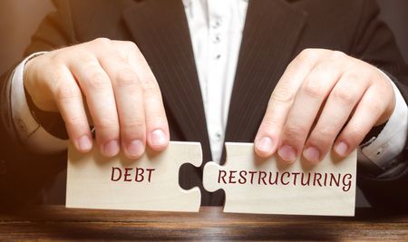 Businessman collects wooden blocks with the word Debt Restructuring. Debts relief. Changing loan repayment terms. Changing the timing and size of payment. Exchange of debt for a share in the propertyの写真素材