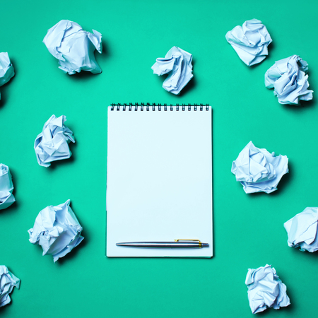 white notebook with pen on a green background among paper balls. The concept of generating ideas, inventing new ideas. Paper balls are all around. Searching of decisions. Bad idea. Businessの写真素材