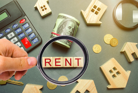 Table with wooden houses, calculator, coins, magnifying glass with the word Rent. The concept of rental housing. Rent an apartment or house. Payment for rent. Real Estate Agent Services. Realtorの写真素材