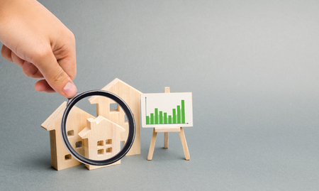 Magnifying glass is looking at the Wooden houses with a stand of graphics and information. Growing demand for housing. growth of city and its population. Investments. rising prices. Selective focusの写真素材
