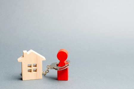 The man is handcuffed to a wooden house. The concept of restriction of freedom due to non-payment of property taxes or mortgage loans. Debt load for housing. Loan. Fine, penalty. Credit.の写真素材